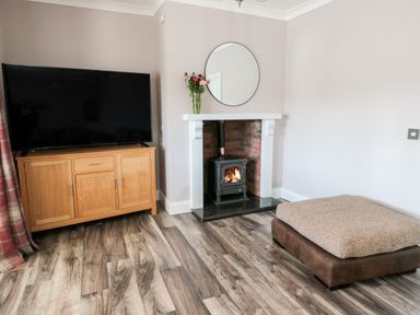A living room with a wood stove fireplace a round mirror on the wall a wooden cabinet with a television and a brown ottoman at Deanrise in Shilbottle near Alnwick
