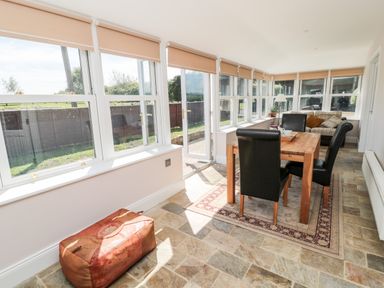 A dining area with a wooden table and black chairs next to large windows and a sofa at Deanrise in Shilbottle near Alnwick