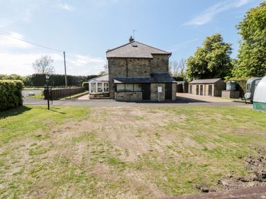 A stone house with a driveway and lawn surrounded by trees and sheds at Deanrise in Shilbottle near Alnwick