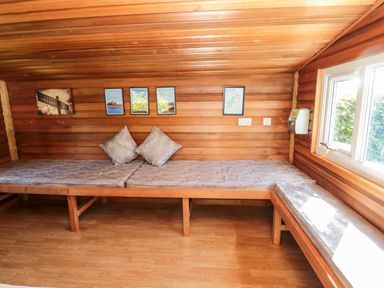 A wooden room with bench seating cushions two pillows and framed pictures on the wall at Deanrise in Shilbottle near Alnwick