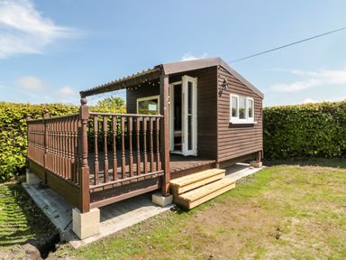 A small wooden cabin with a covered porch and steps in a garden at Deanrise in Shilbottle near Alnwick