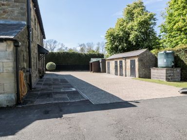 An outdoor area with a stone building on the left a paved courtyard stone storage sheds and trees at Deanrise Shilbottle near Alnwick