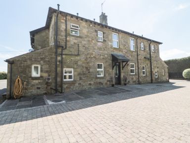 A stone exterior of a two-story building with multiple windows and a black door canopy at Deanrise in Shilbottle near Alnwick