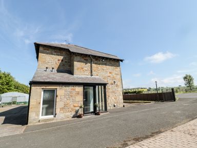 A stone house with a slate roof on a paved area with a gated fence and countryside beyond at Deanrise in Shilbottle near Alnwick