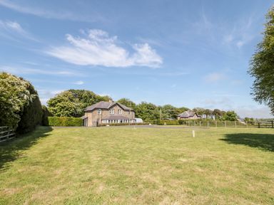 A large grassy yard with two stone houses surrounded by trees and fences at Deanrise in Shilbottle near Alnwick