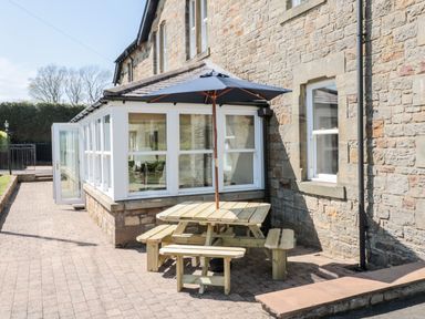 An outdoor picnic table with an umbrella next to a stone house and sunroom at Deanrise in Shilbottle near Alnwick