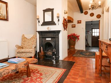 A room with a floral armchair a wooden coffee table books a fireplace a mirror wall sconces a hallway with a rug and a wooden door at Harbour Cottage in Watchet
