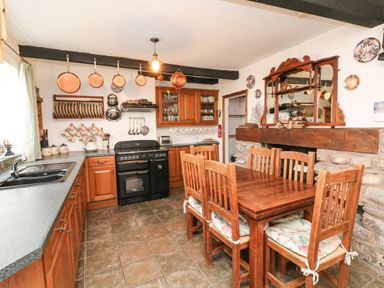 A kitchen with wooden cabinets a black stove copper pans hanging above and a wooden dining table with six chairs at Harbour Cottage in Watchet