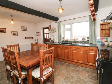 A kitchen with wooden cabinets a dining table and chairs and a window with curtains at Harbour Cottage in Watchet