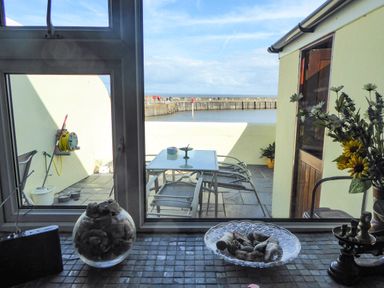 A balcony with a table and chairs overlooking a harbor with a yellow wall and mop nearby at Harbour Cottage in Watchet