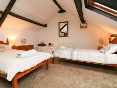 A bedroom with two single beds wooden furniture a mirror and slanted ceiling at Harbour Cottage in Watchet