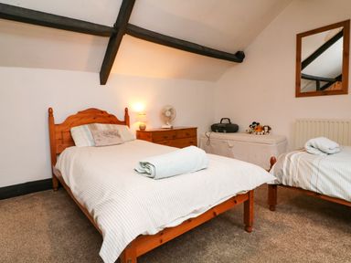 A bedroom with two single beds a wooden dresser with a lamp and fan and a mirror on the wall at Harbour Cottage in Watchet