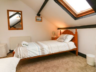 A bedroom with a single bed striped bedding a wooden headboard a skylight window a bedside table with a lamp and fan a mirror and radiator on the wall at Harbour Cottage in Watchet
