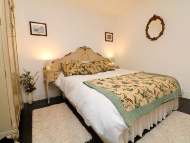 A bedroom with a double bed with floral bedding two bedside tables with lamps a wardrobe a floral vase and framed pictures on the walls at Harbour Cottage in Watchet