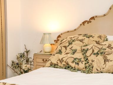 A bed with floral patterned cushions and a nightstand with a lamp and flowers at Harbour Cottage in Watchet
