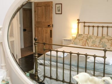 A bedroom with a brass bed and floral pillows seen in a round mirror at Harbour Cottage in Watchet