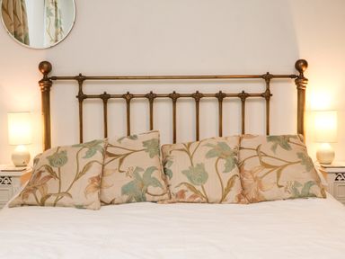 A bed with a metal headboard four floral patterned pillows two bedside tables each with a lamp and a round mirror on the wall at Harbour Cottage in Watchet