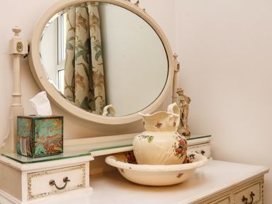 A vanity table with a round mirror a tissue box a floral pitcher and basin and a figurine at Harbour Cottage in Watchet