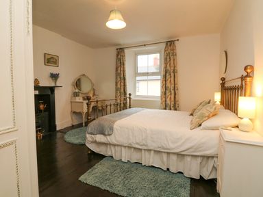 A bedroom with a brass bed a vanity table a fireplace and window with curtains at Harbour Cottage in Watchet