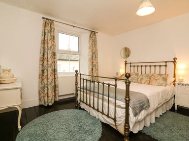 A bedroom with a brass bed frame floral curtains bedside tables and round rugs at Harbour Cottage in Watchet