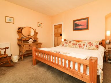 A bedroom with a wooden bed and floral bedding a wooden dressing table and rocking chair at Harbour Cottage in Watchet