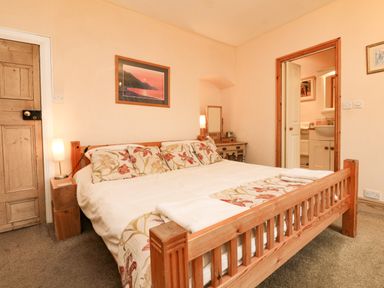 A bedroom with a wooden bed a bedside lamp a dressing table and an open door showing a bathroom at Harbour Cottage in Watchet
