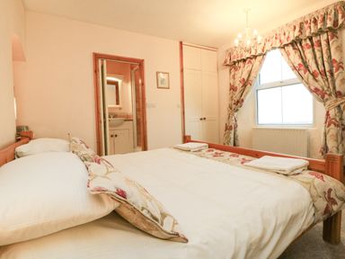 A bedroom with a double bed white bedding floral curtains wooden wardrobe and an ensuite bathroom at Harbour Cottage in Watchet
