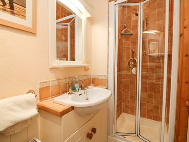 A bathroom with a white sink and mirror next to a shower with tiled walls at Harbour Cottage in Watchet