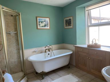 A bathroom with a clawfoot bathtub a glass shower wooden cabinet and two framed pictures on the wall at Harbour Cottage in Watchet