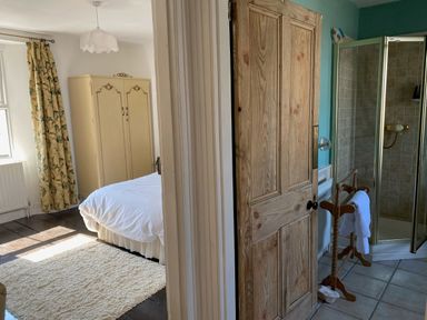 A bedroom with a bed wardrobe and curtain next to a bathroom with a shower and towel rack at Harbour Cottage Watchet