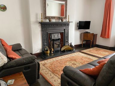 A living room with a black fireplace a mirror above it two sofas a television on a wooden stand and an orange patterned rug at Harbour Cottage in Watchet