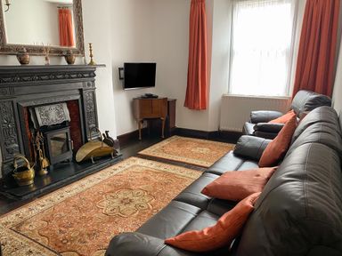 A living room with a black fireplace a wall mounted TV leather sofas orange cushions and curtains at Harbour Cottage in Watchet