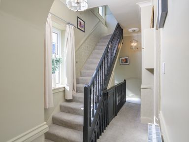 A carpeted stairway with black banisters and a window with curtains in a hallway at Ferrystone Kingswear near Dartmouth