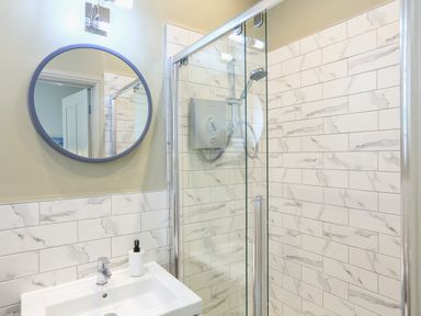 A bathroom shower area with tiled walls a round mirror a sink and a soap dispenser at Ferrystone Kingswear near Dartmouth