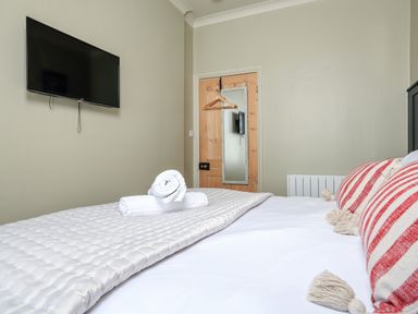A bedroom with a bed with red and white striped pillows rolled towels on the bed a wall mounted television and a door with a mirror at Ferrystone Kingswear near Dartmouth