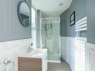 A bathroom with a sink, round mirror, shower enclosure, and towel radiator at Ferrystone Kingswear near Dartmouth