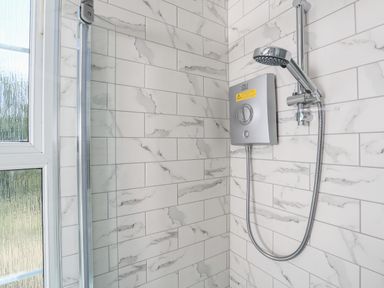 A corner shower with a handheld showerhead and control panel on tiled walls next to a frosted window at Ferrystone in Kingswear near Dartmouth
