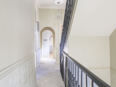A hallway with carpeted floor and black stair railing leading to an arched doorway with a view of kitchen cabinets at Ferrystone Kingswear near Dartmouth