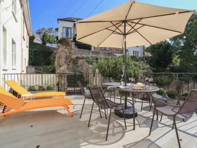 An outdoor patio with orange lounge chairs a table with chairs and a large umbrella at Ferrystone Kingswear near Dartmouth