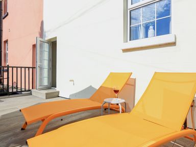 Two orange lounge chairs on a wooden deck with a small white table holding a glass of red wine at Ferrystone Kingswear near Dartmouth