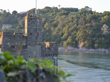 A stone castle tower by a river with trees on the opposite bank at Ferrystone in Kingswear near Dartmouth