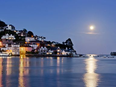 A coastal village at dusk with houses lit along the hillside and boats on the water at Ferrystone Kingswear near Dartmouth