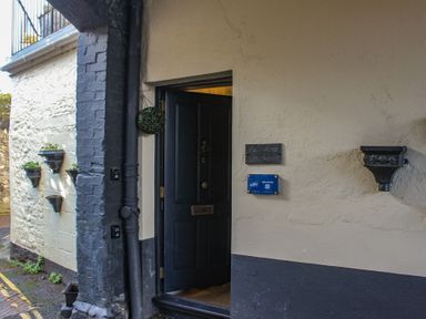 An open black door on a building with cream and black walls and small potted plants on the exterior wall at Ferrystone in Kingswear near Dartmouth