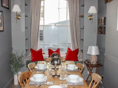 A dining room with a wooden table set for six near a window with red cushions at Ferrystone in Kingswear near Dartmouth