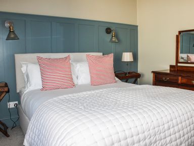 A bedroom with a bed with striped pillows beside bedside tables and a dresser with mirror at Ferrystone Kingswear near Dartmouth
