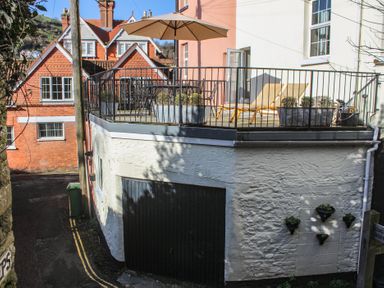 An outdoor terrace with patio furniture and an umbrella above a garage door at Ferrystone in Kingswear near Dartmouth