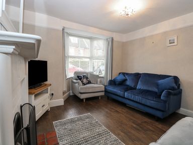 A living room with a blue sofa a grey armchair a television on a stand and a fireplace at Hunny Cottage in Hunstanton