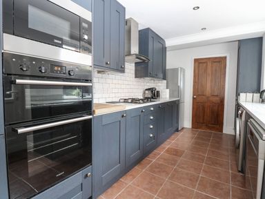 A kitchen with blue cabinets white countertops tiled floor and wooden door at Hunny Cottage Hunstanton