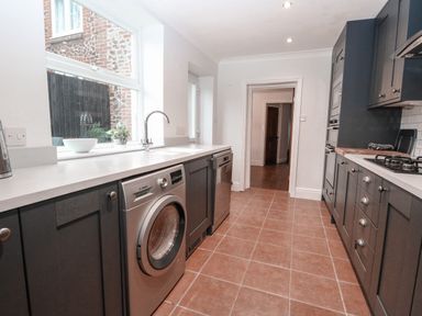 A kitchen with dark cabinets white countertops a washing machine a dishwasher a sink a gas stove and a window with a view at Hunny Cottage in Hunstanton