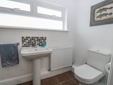 A bathroom with a white pedestal sink, a toilet, a blue towel on a rail, and a fish painting on the wall at Hunny Cottage in Hunstanton